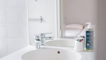 A bathroom with a white sink, a mirror, a hairdryer, and a bottle of hotel-branded shampoo.