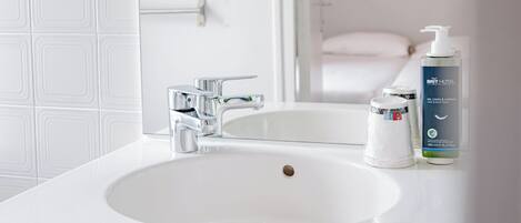 A bathroom with a white sink, a mirror, a hairdryer, and a bottle of hotel-branded shampoo.