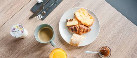Un desayuno con un croissant, queso, mermelada en un plato, una taza de café, un frasco pequeño de mermelada y un envase de yogur.