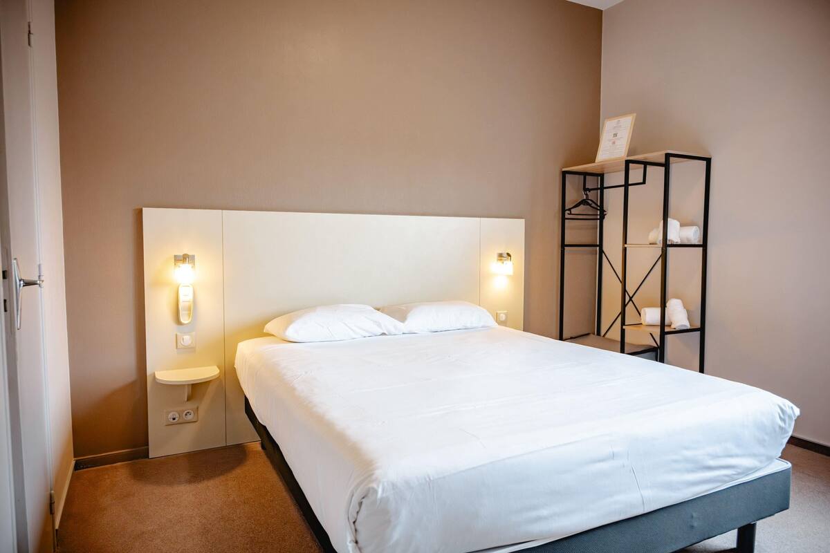 A hotel room with a large bed, bedside lamps, a small bedside table, and a wardrobe with hanging space.