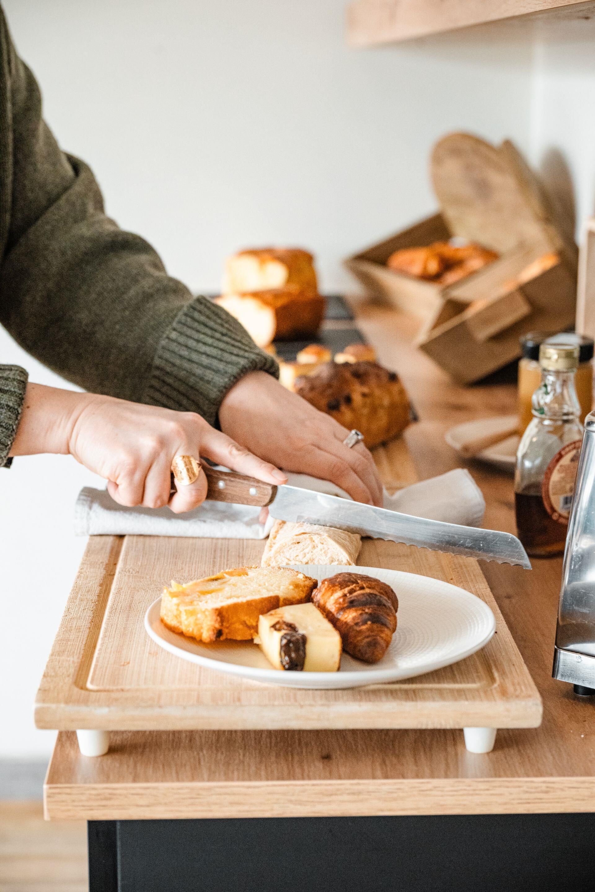 A person slicing bread on a wooden cutting board.