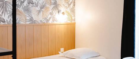 A room with a bunk bed, a bedside table, a small desk, and a wall with a tropical leaf pattern.