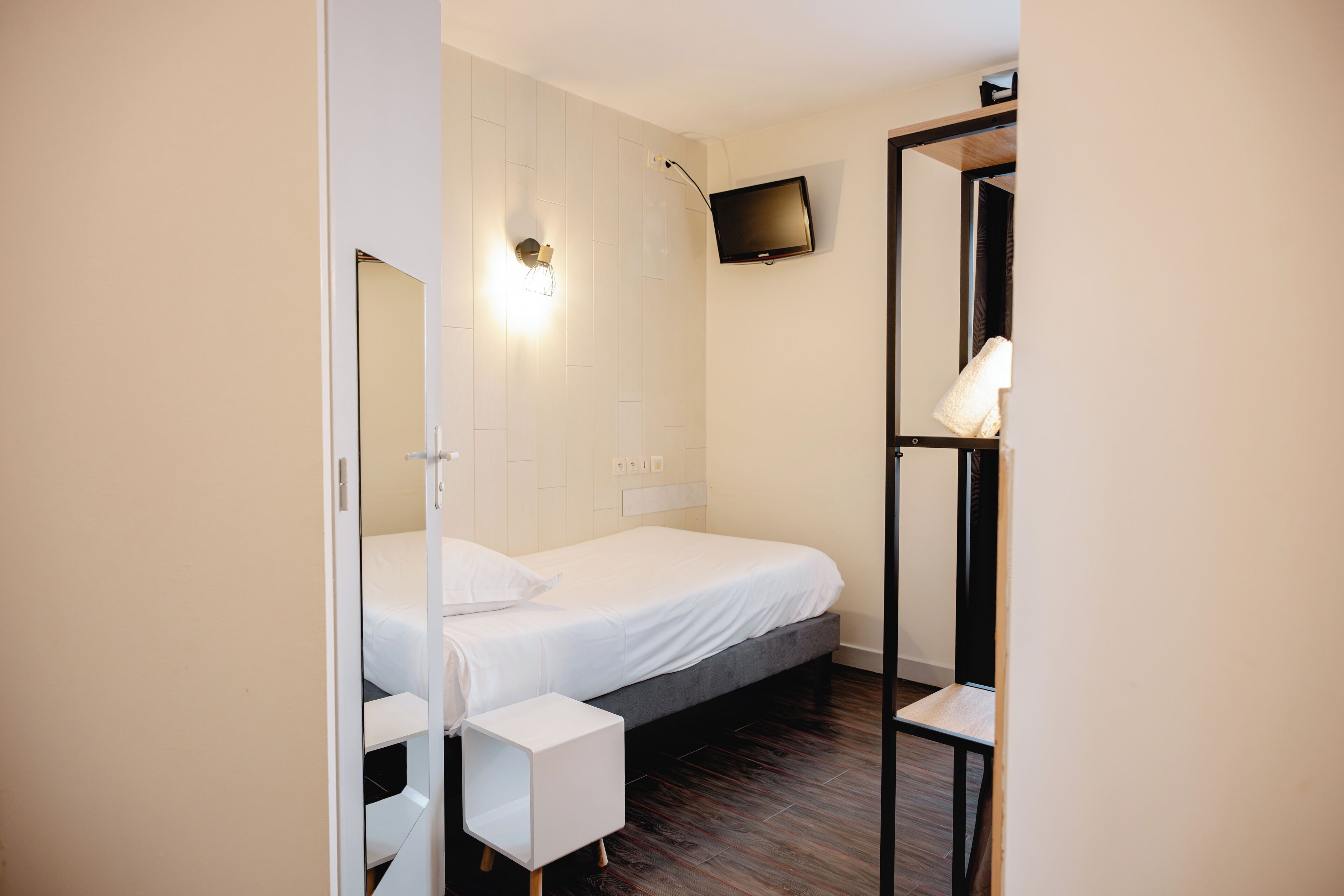 Een slaapkamer met een bed, nachtkastje en een aan de muur bevestigde televisie.