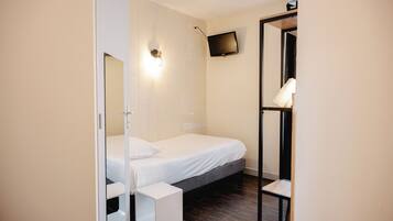 Een slaapkamer met een bed, nachtkastje en een aan de muur bevestigde televisie.