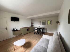 Una sala moderna con un sofá, una mesa de comedor con sillas, una zona de cocina con mostrador y un televisor de pantalla plana montado en la pared.