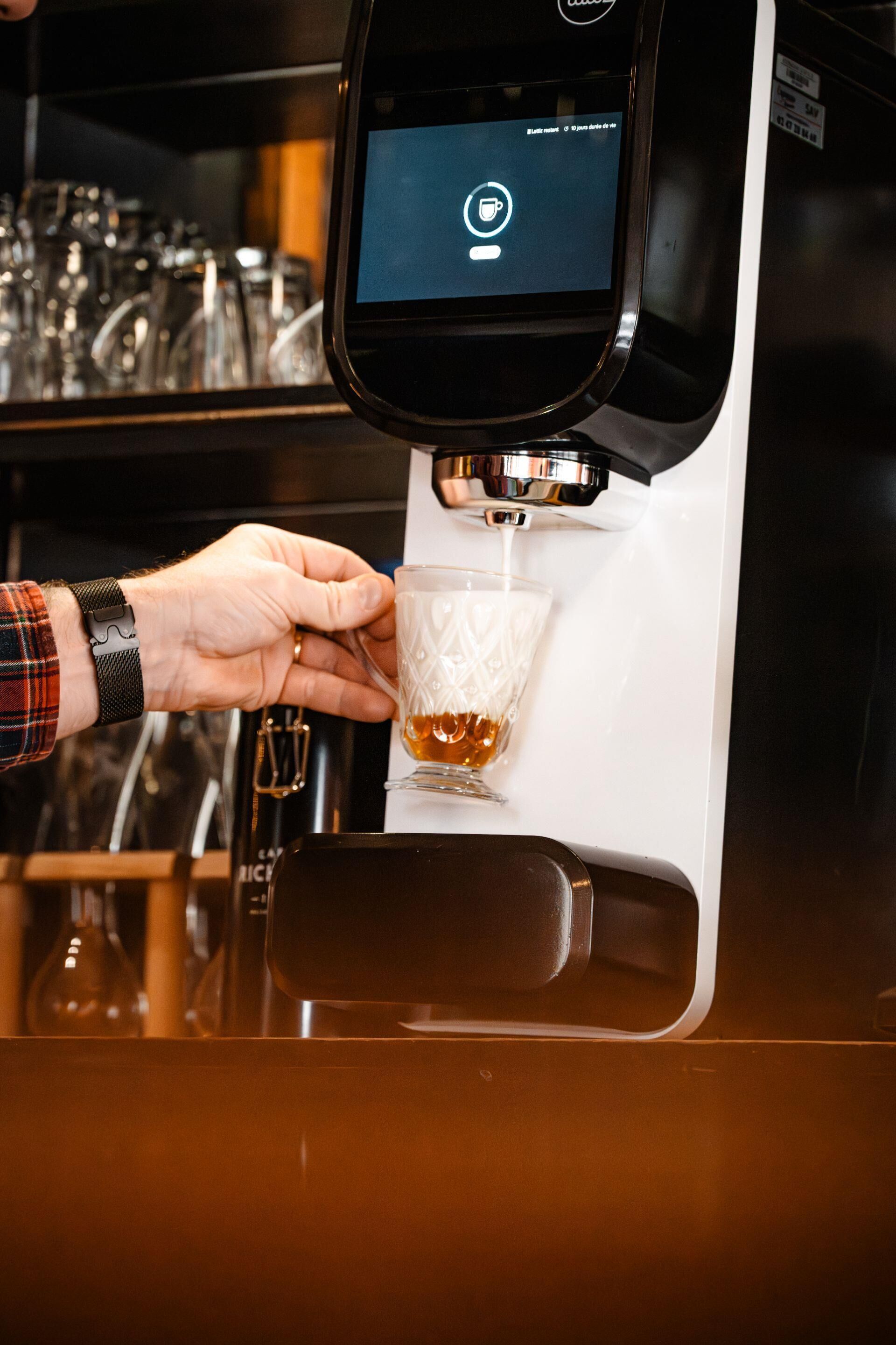 A person using a coffee machine to fill a glass with coffee.