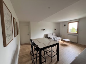 A modern living space with a dining area, a sofa, a window with a view, and wall-mounted artwork. - Brit Hotel L'Arrivée Guingamp (Guingamp)