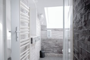 A modern bathroom with a glass shower enclosure, a white radiator, and a stone wall backsplash. - Brit Hotel L'Arrivée Guingamp (Guingamp)