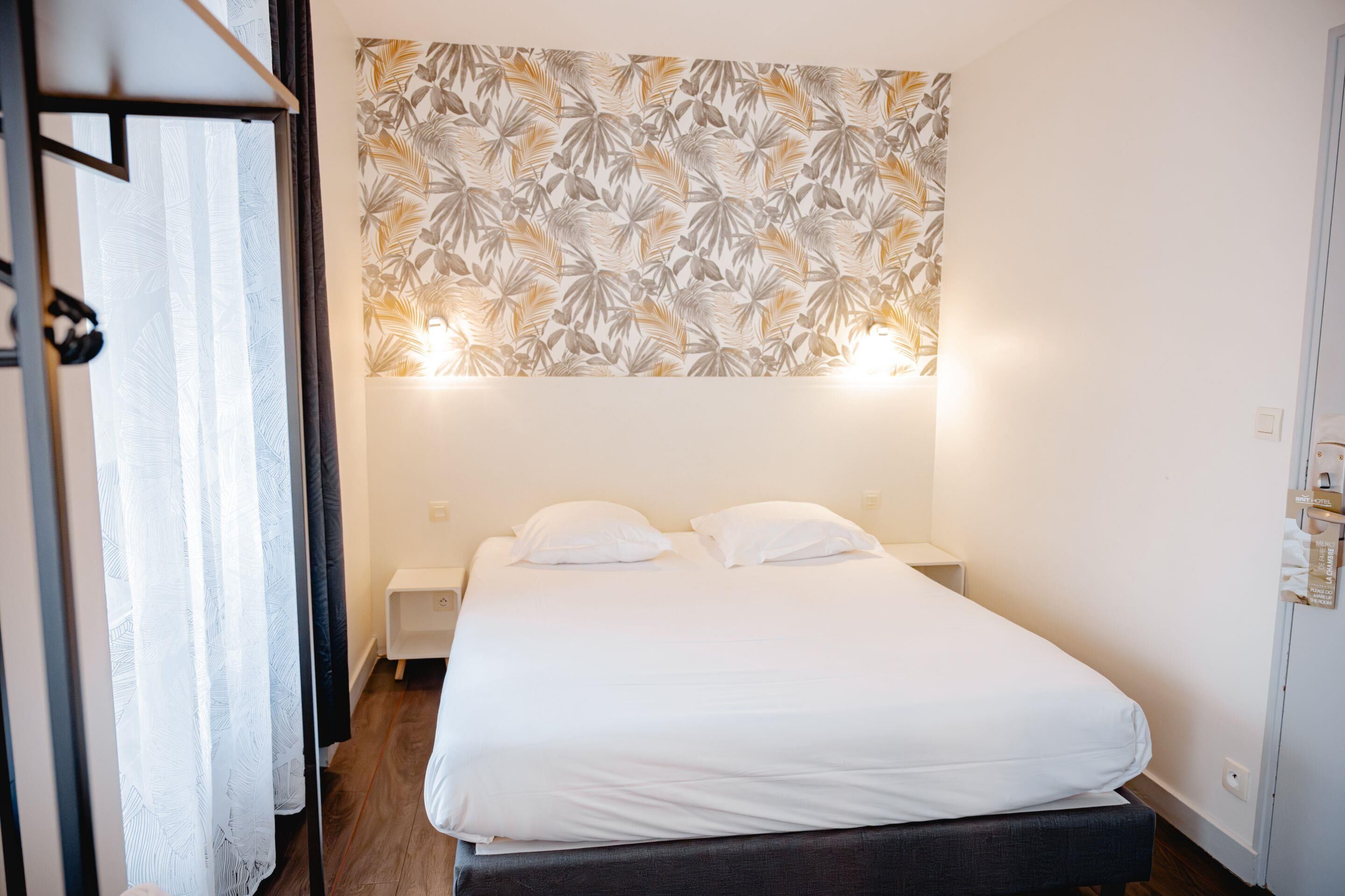 A neatly made bed with white bedding in a room with a tropical leaf-patterned wall.