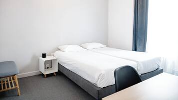 Ein Hotelzimmer mit zwei Einzelbetten, einem kleinen Nachttisch, einem Stuhl und einem Schreibtisch.