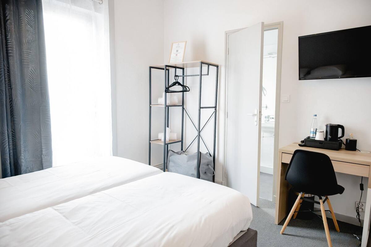 A hotel room with a bed, a desk with a chair, a TV, and a wardrobe.