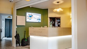 A reception desk with multilingual welcome signs, a green wall, and a ceiling-mounted security camera.