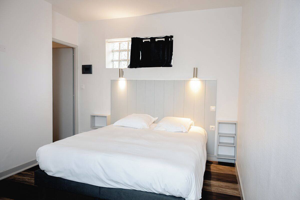 A bedroom with a bed, a window with curtains, and a wall-mounted light fixture.