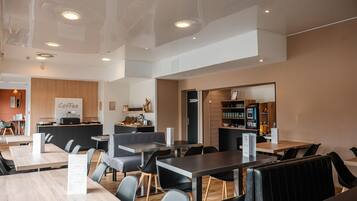 A modern cafe with wooden tables and black chairs, a coffee bar, and a menu board.