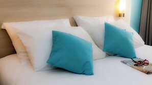 A hotel room with a wooden headboard, white bedding, and two teal pillows. - Brit Hotel La Rochelle Périgny (Perigny)