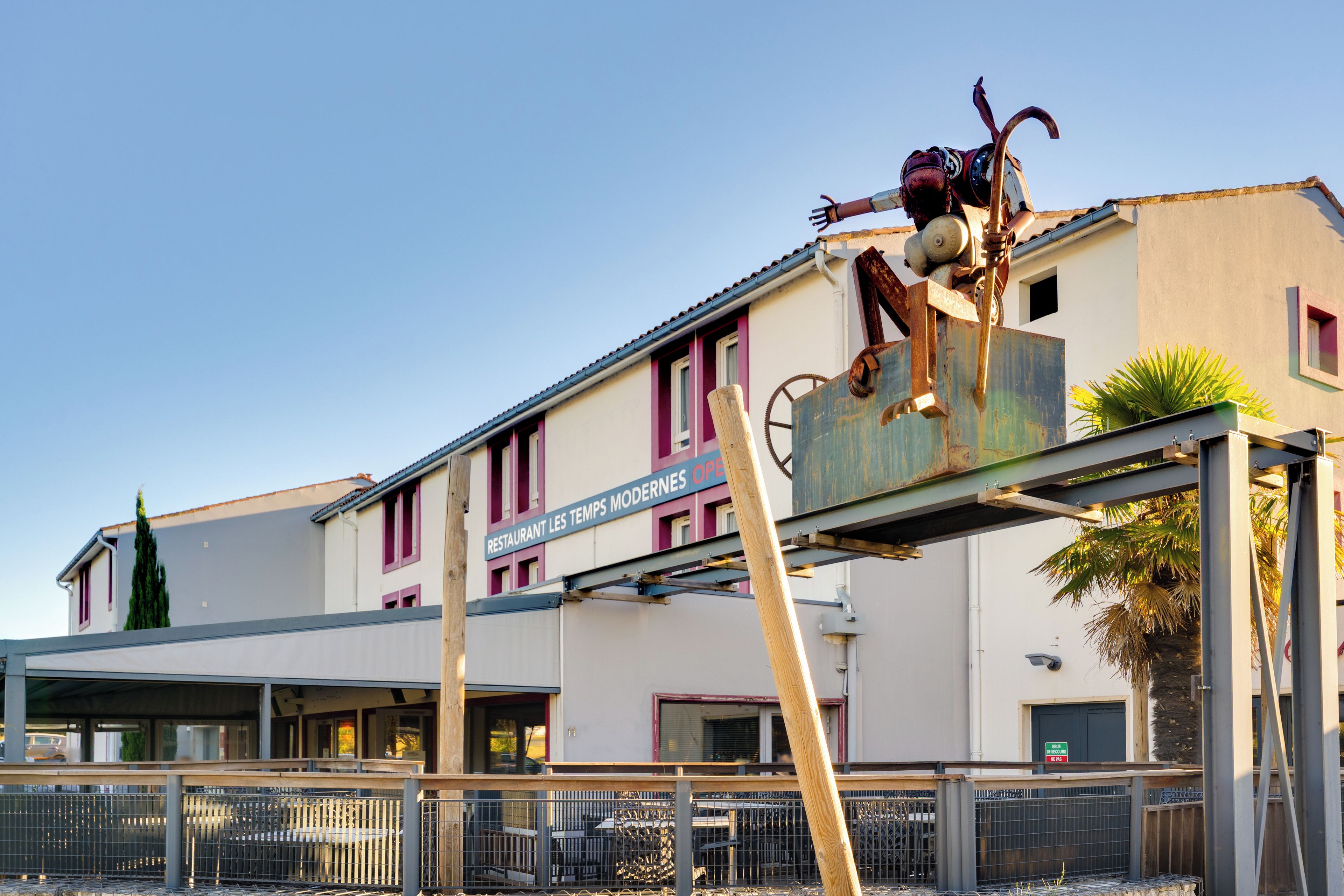 Un bâtiment avec une enseigne indiquant « RESTAURANT LES TEMPS MODERNES OUVERT » et une structure métallique devant.
