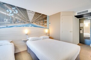 Habitación de hotel con una cama grande, una mesita de noche, una lámpara de pared y una puerta que da a un baño.