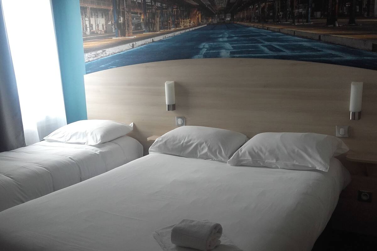 A hotel room with two beds, a large window, and a view of a city street.