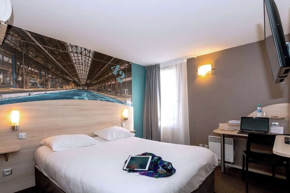 A hotel room with a bed, bedside lamps, a desk with a laptop, a water bottle, and a large mural of a bridge.