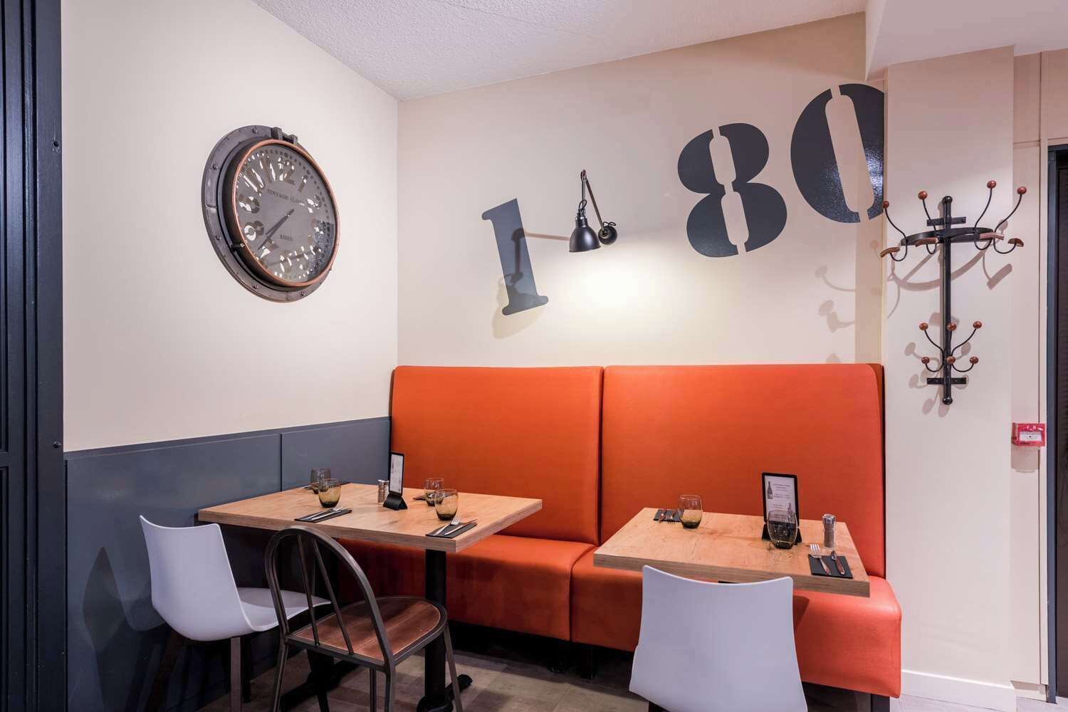 A modern interior with a large clock, orange seating, and a wall-mounted coat rack.