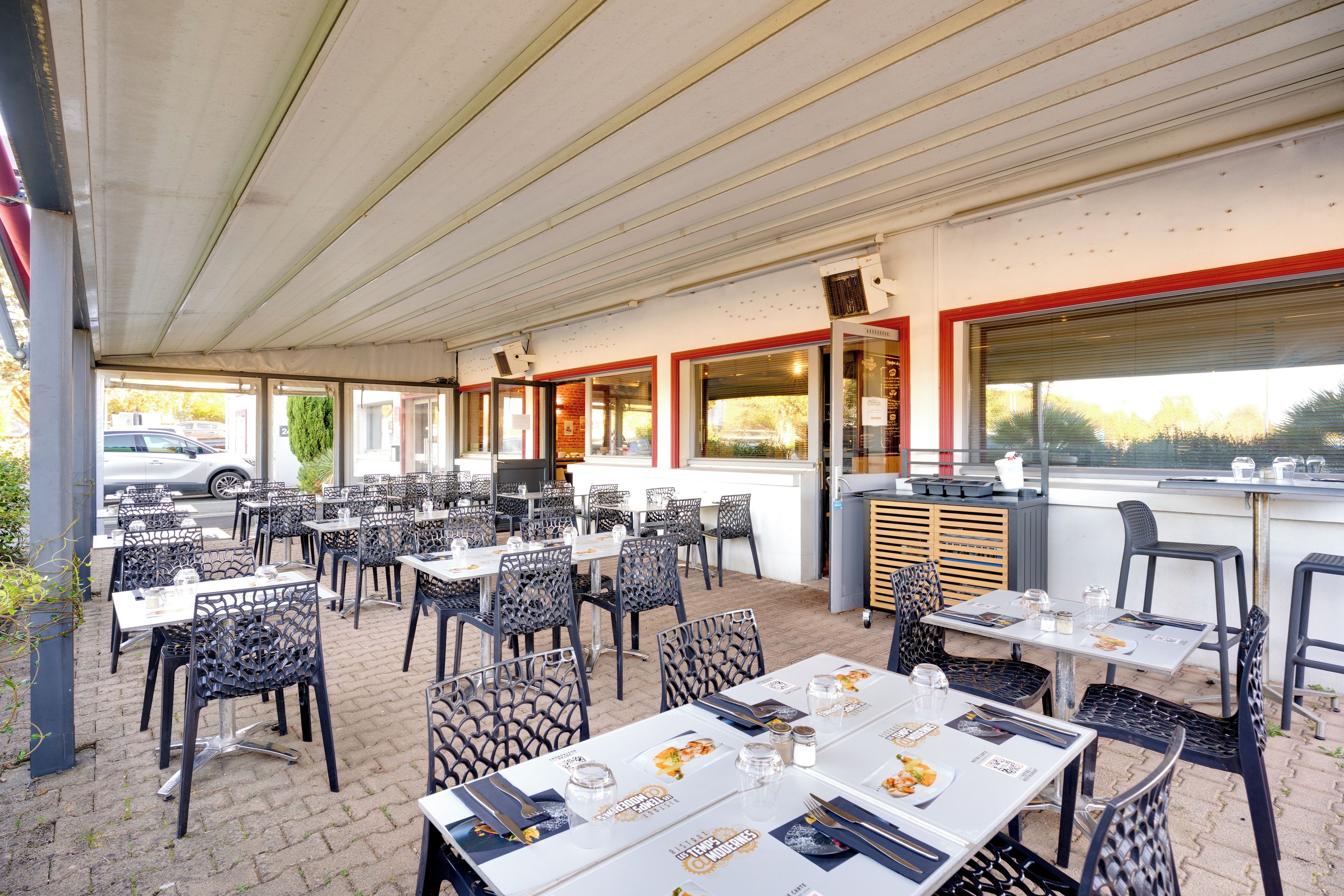 Un'area pranzo all'aperto con tavoli e sedie, un tetto coperto e vista sulla strada.