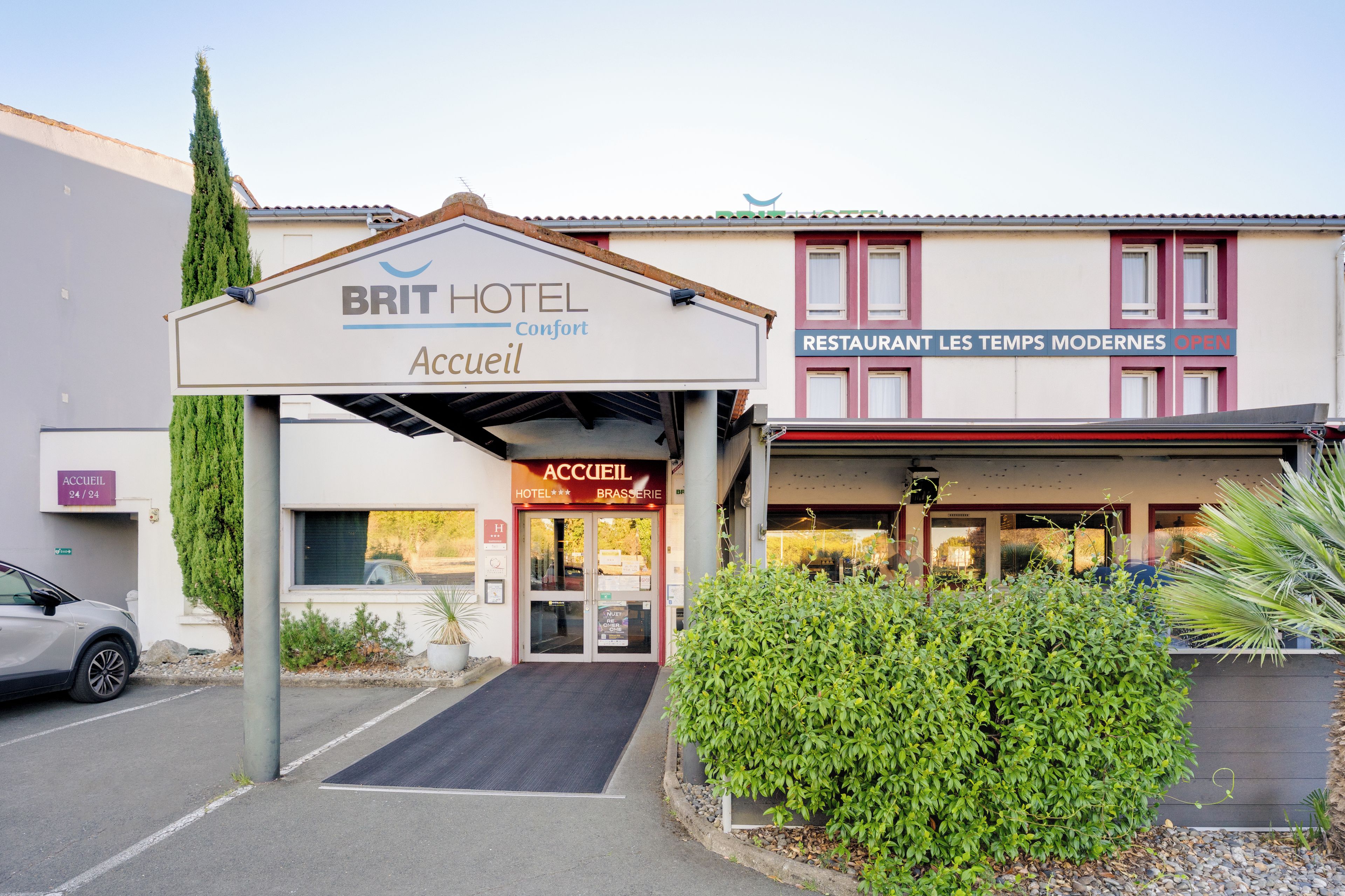 A hotel entrance with a sign for 'BRIT HOTEL Accueil' and a restaurant named 'RESTAURANT LES TEMPS MODERNES OPEN'.