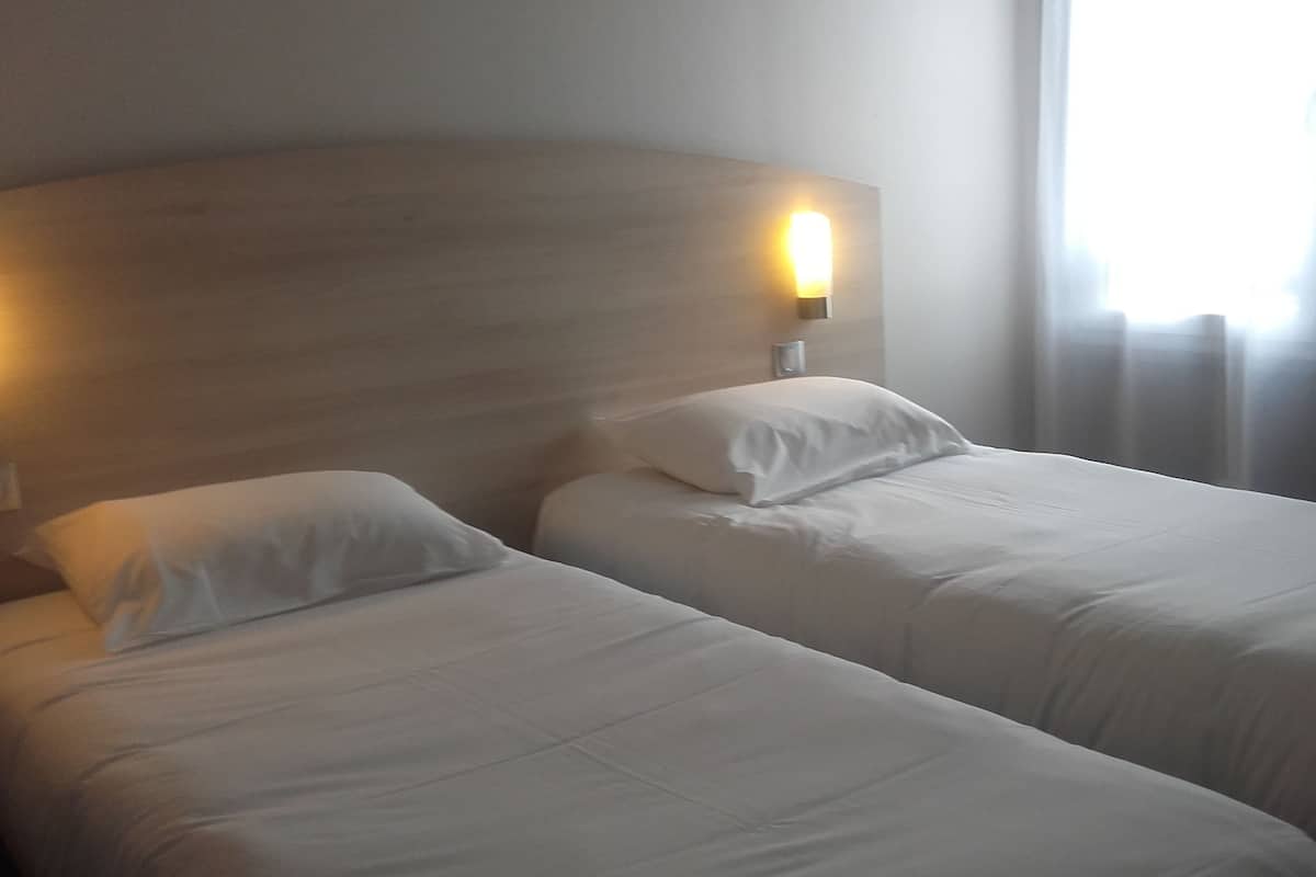 A hotel room with two single beds, a wooden headboard, and a bedside lamp.