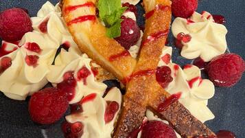 A dessert plate with a pastry, whipped cream, raspberries, and a mint leaf.