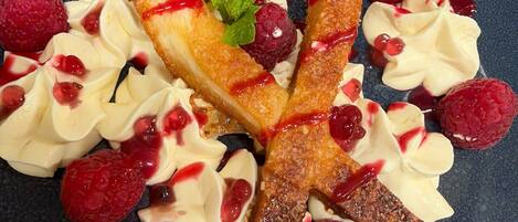 Un plato de postre con un pastel, crema batida, frambuesas y una hoja de menta.