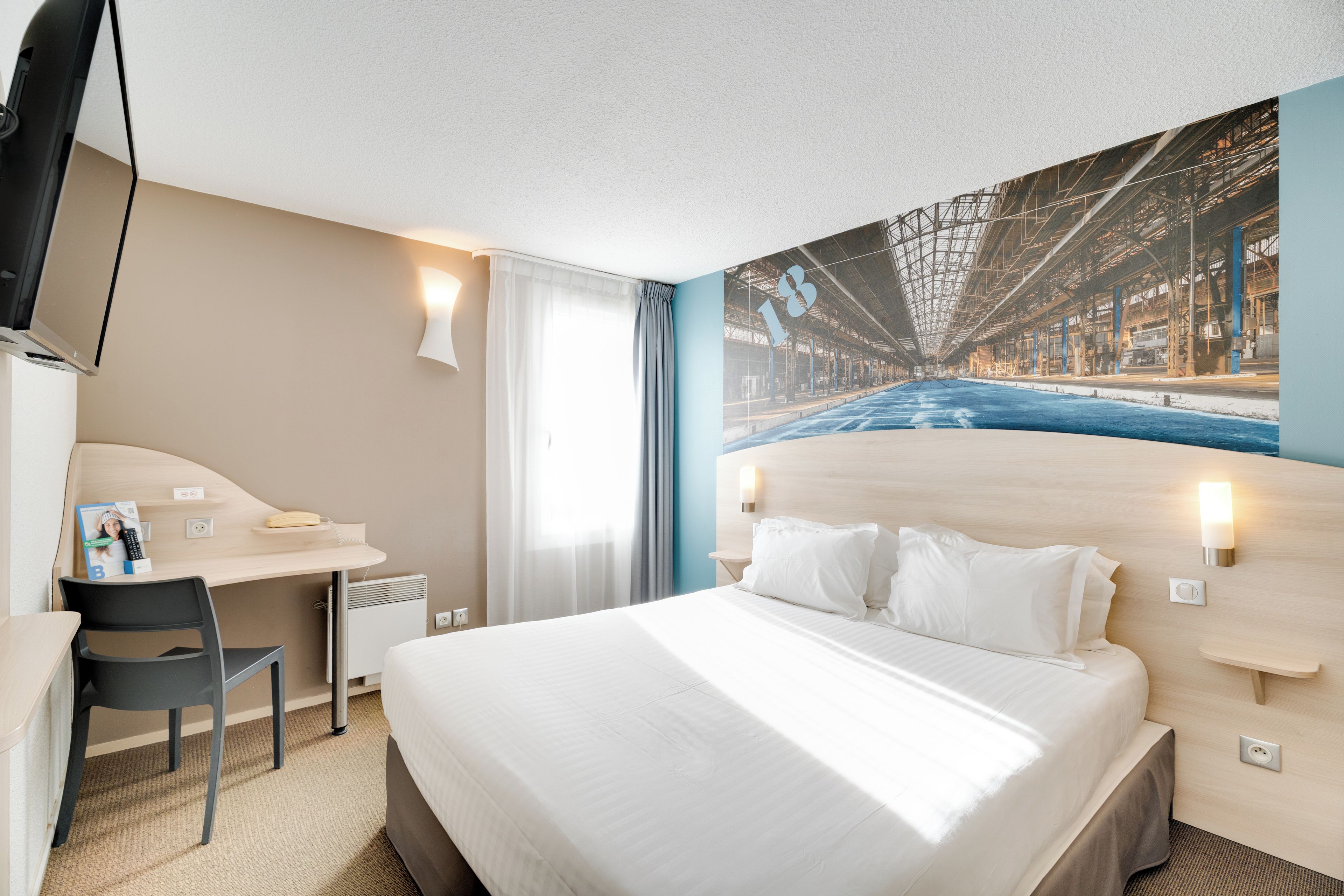 A hotel room with a bed, a desk, a chair, a television, and a large window.