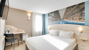 Una habitación de hotel con cama, escritorio, silla, televisor y ventana grande.