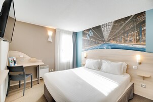 Una habitación de hotel con cama, escritorio, silla, televisor y ventana grande.