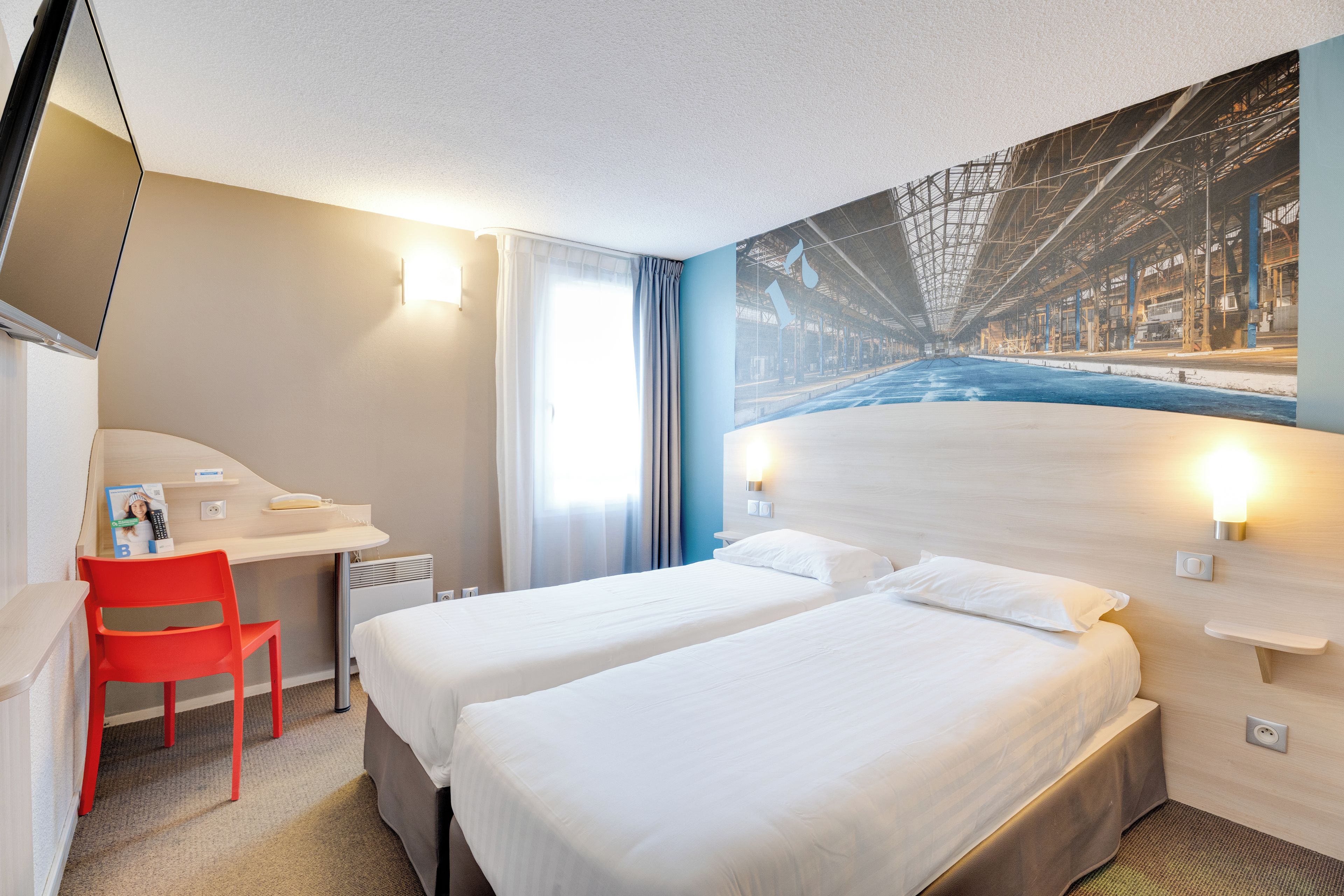 Habitación de hotel con dos camas, un escritorio, una silla y un ventanal grande.