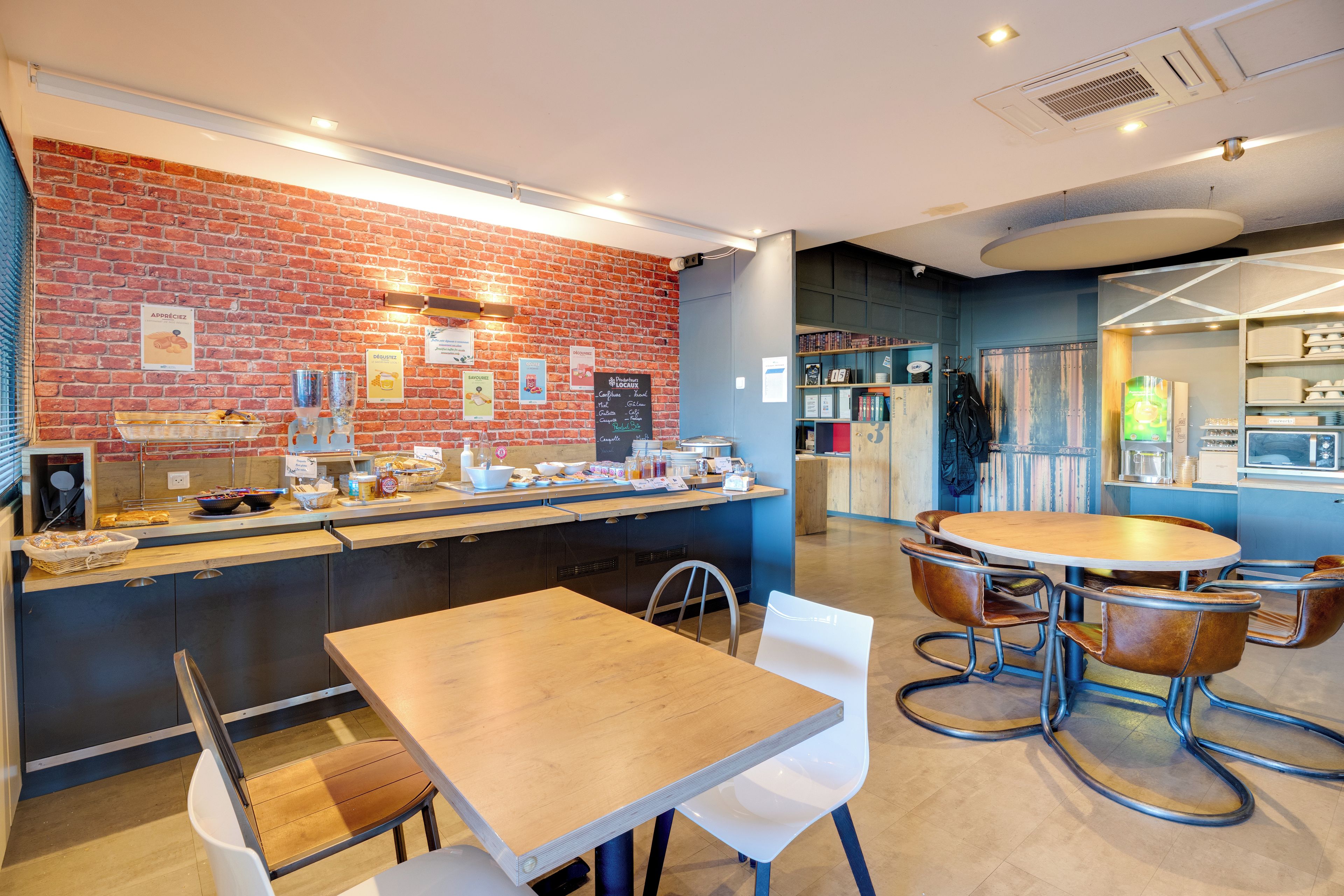 Un café avec un mur en briques, un comptoir en bois et un espace salon avec des tables et des chaises.