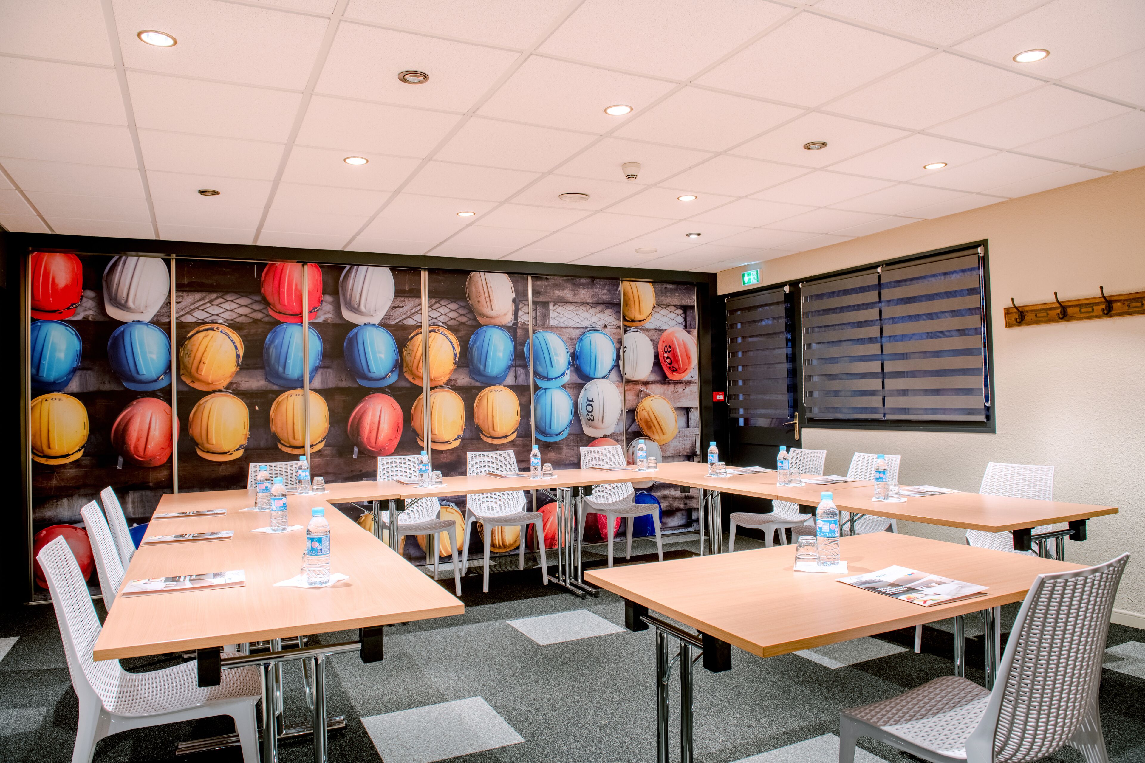 A conference room with tables and chairs, a wall mural, and a window with blinds.