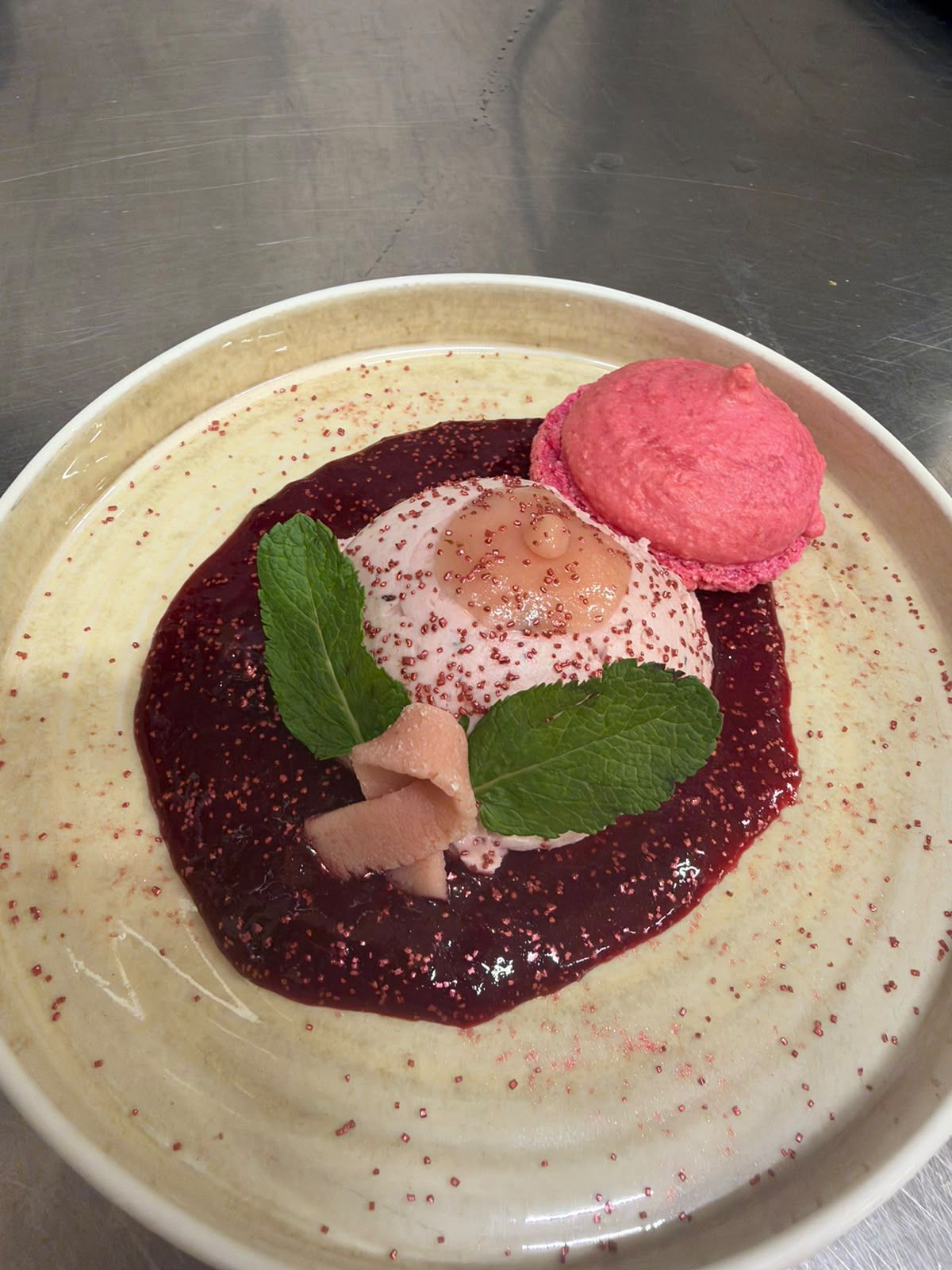 A dessert plate with a scoop of pink ice cream, a piece of what appears to be a fruit compote, and a mint leaf garnish.