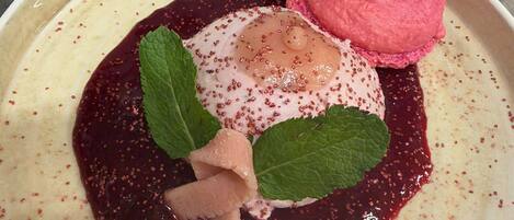 Un plato de postre con una porción de helado rosa, un poco de compota de frutas y una hoja de menta como adorno.