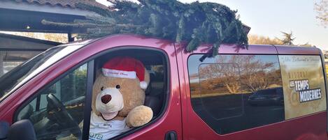 Un fourgon rouge dans lequel est assis, sur le siège passager, un grand ours en peluche portant un bonnet de Père Noël.