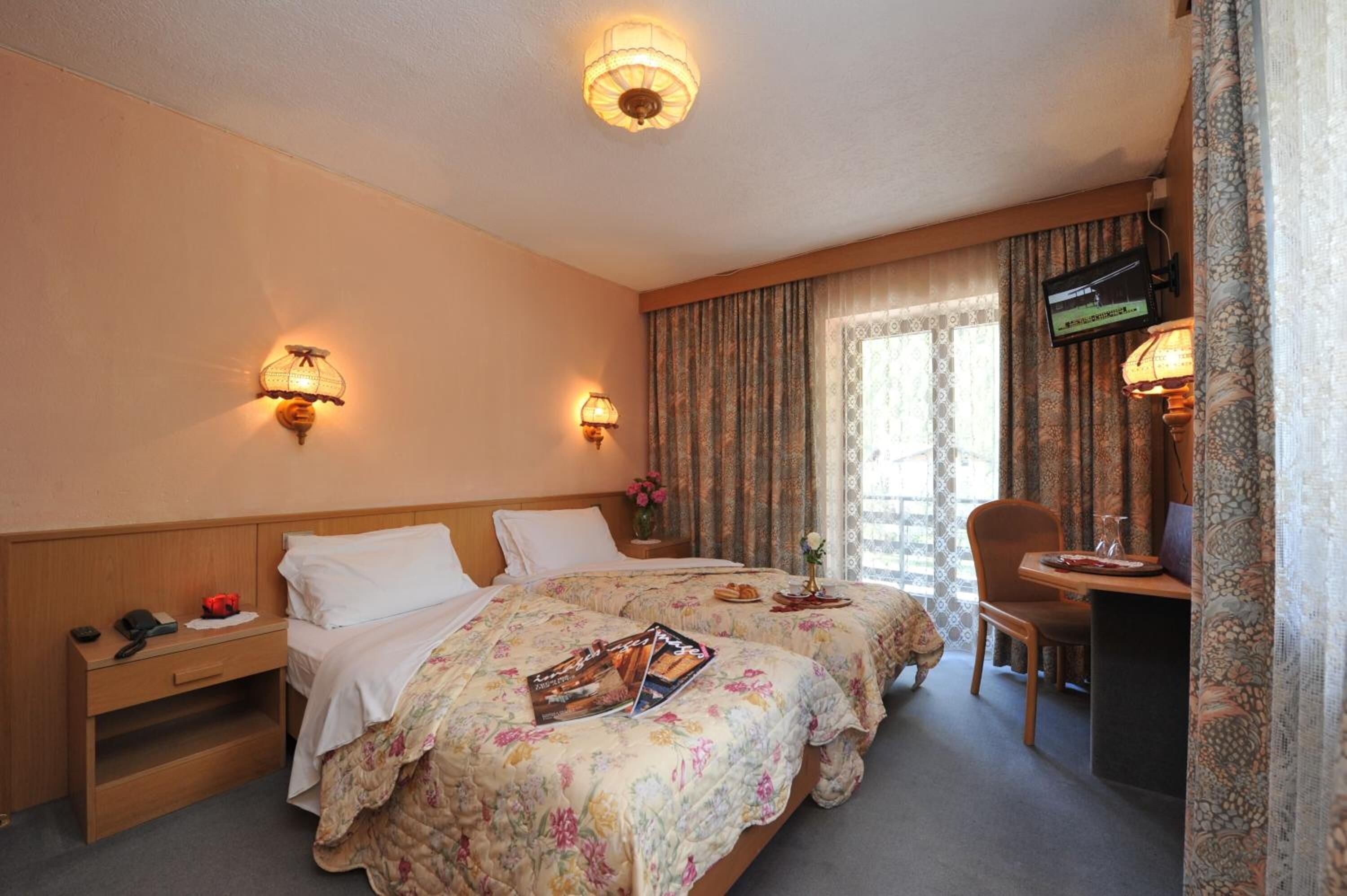 Une chambre d’hôtel avec deux lits, un bureau avec une chaise, une télévision et une fenêtre avec des rideaux.