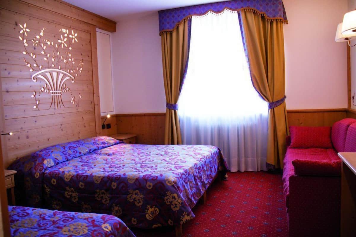 A room with two beds, a wooden wall with a floral design, a window with yellow curtains, and a red carpet.