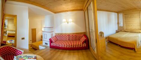 A cozy room with a wooden ceiling, a bed, a red sofa, a small table with magazines, and a mirror.