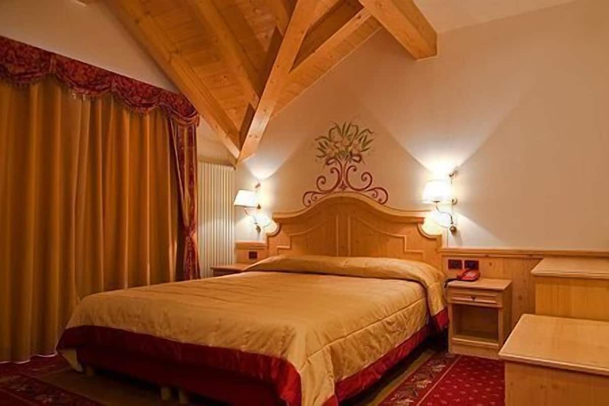 A bedroom with a wooden ceiling, a bed with a red bedspread, two bedside lamps, and a nightstand with a lamp.