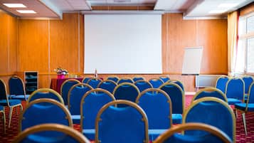 Un salón de conferencias con filas de sillas azules, una pizarra y una pantalla de proyector.