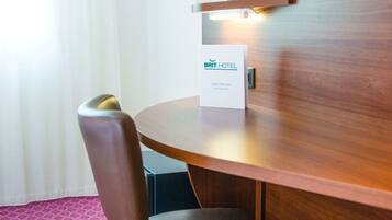 A hotel room with a wooden desk, a chair, a water bottle, and a sign indicating the room type.