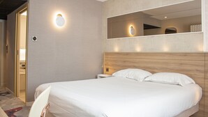 Ein Hotelzimmer mit einem großen Bett, einem Nachttisch, einem an der Wand befestigten Spiegel und einer Tür zu einem Badezimmer.