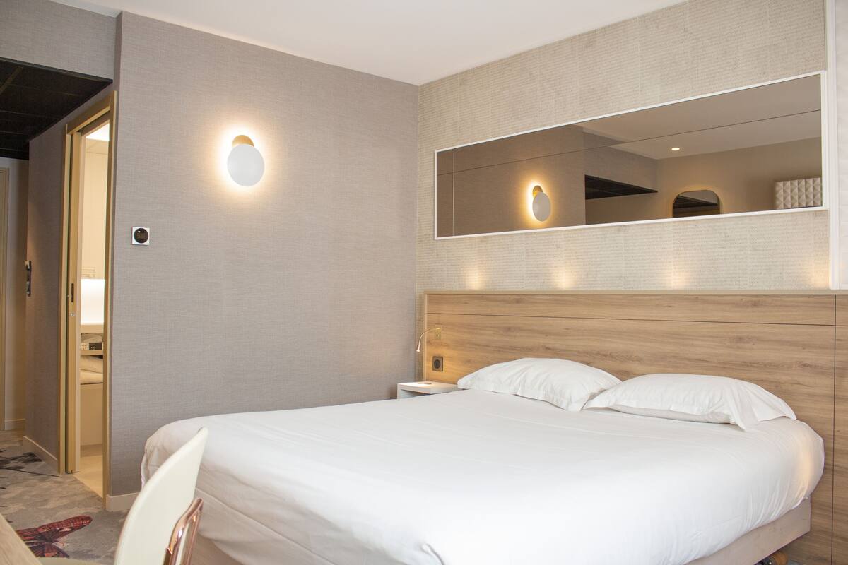 Ein Hotelzimmer mit einem großen Bett, einem Nachttisch, einem an der Wand befestigten Spiegel und einer Tür zu einem Badezimmer.
