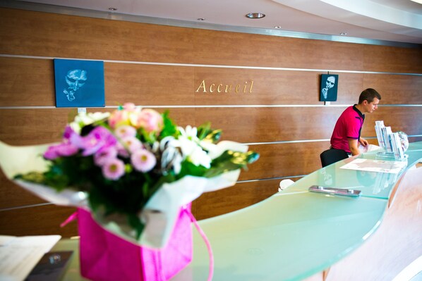 Un mostrador de recepción con encimera de vidrio, un ramo de flores y un cartel que dice 'Accueil'.