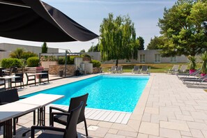 A swimming pool with lounge chairs and tables, surrounded by a brick patio and greenery. - Brit Hotel Nantes Vigneux - L'Atlantel (Vigneux-de-Bretagne)