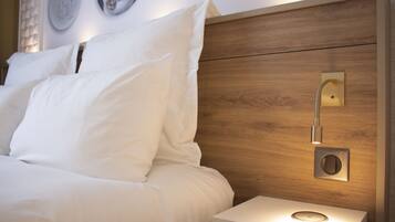 Un lit bien fait, avec du linge de lit blanc, une tête de lit en bois, une table de chevet avec une lampe et un luminaire fixé au mur.