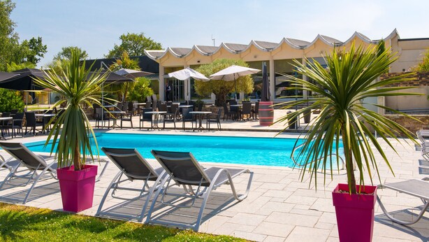 Ein Poolbereich mit Liegestühlen, Sonnenschirmen und einem Gebäude mit markanter Dachlinie.